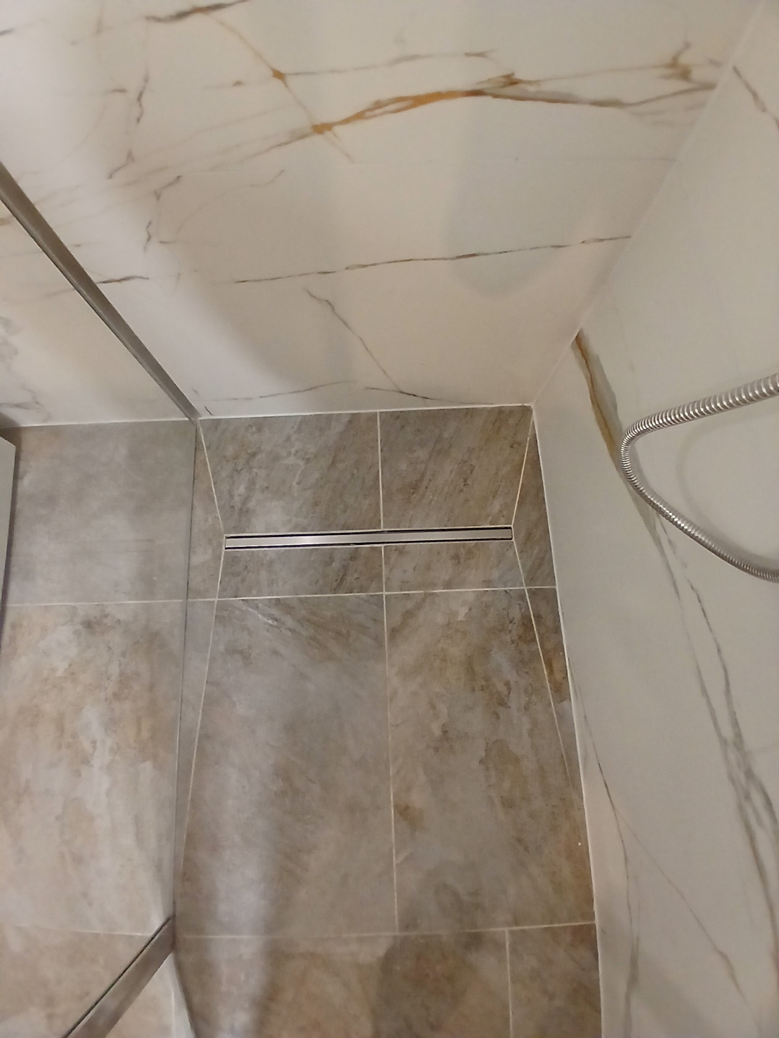 Wykończona strefa prysznicowa z odpływem liniowym i marmurowymi płytkami. Widoczne detale wykończenia i armatura. Minimalistyczny design.