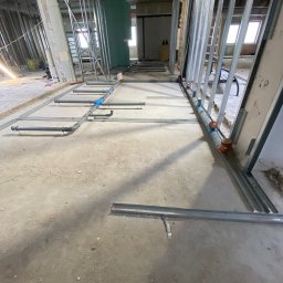 MP Hydro-Went Systems Mykhailo Pidhorodetskyi - Instalacja rur kanalizacyjnych w surowym wnętrzu budynku w Poznaniu. Widoczne szare rury i metalowe profile konstrukcyjne ścian działowych. Etap prac instalacyjnych.