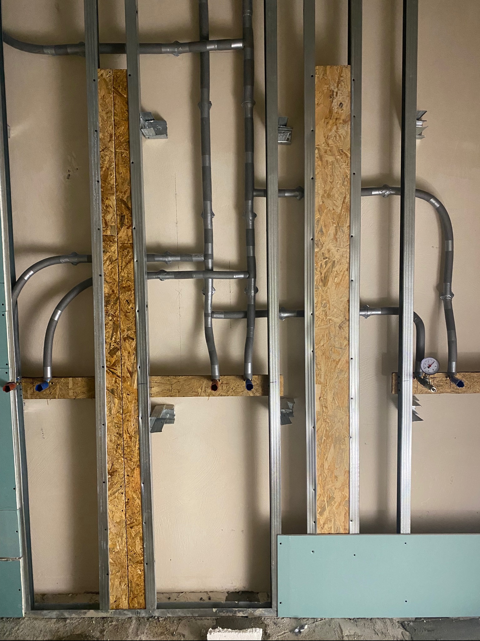 Instalacja rur w ścianie z płyt OSB i metalowych profili. Widoczne rury, mocowania i manometr. Etap prac instalacyjnych wewnątrz budynku.