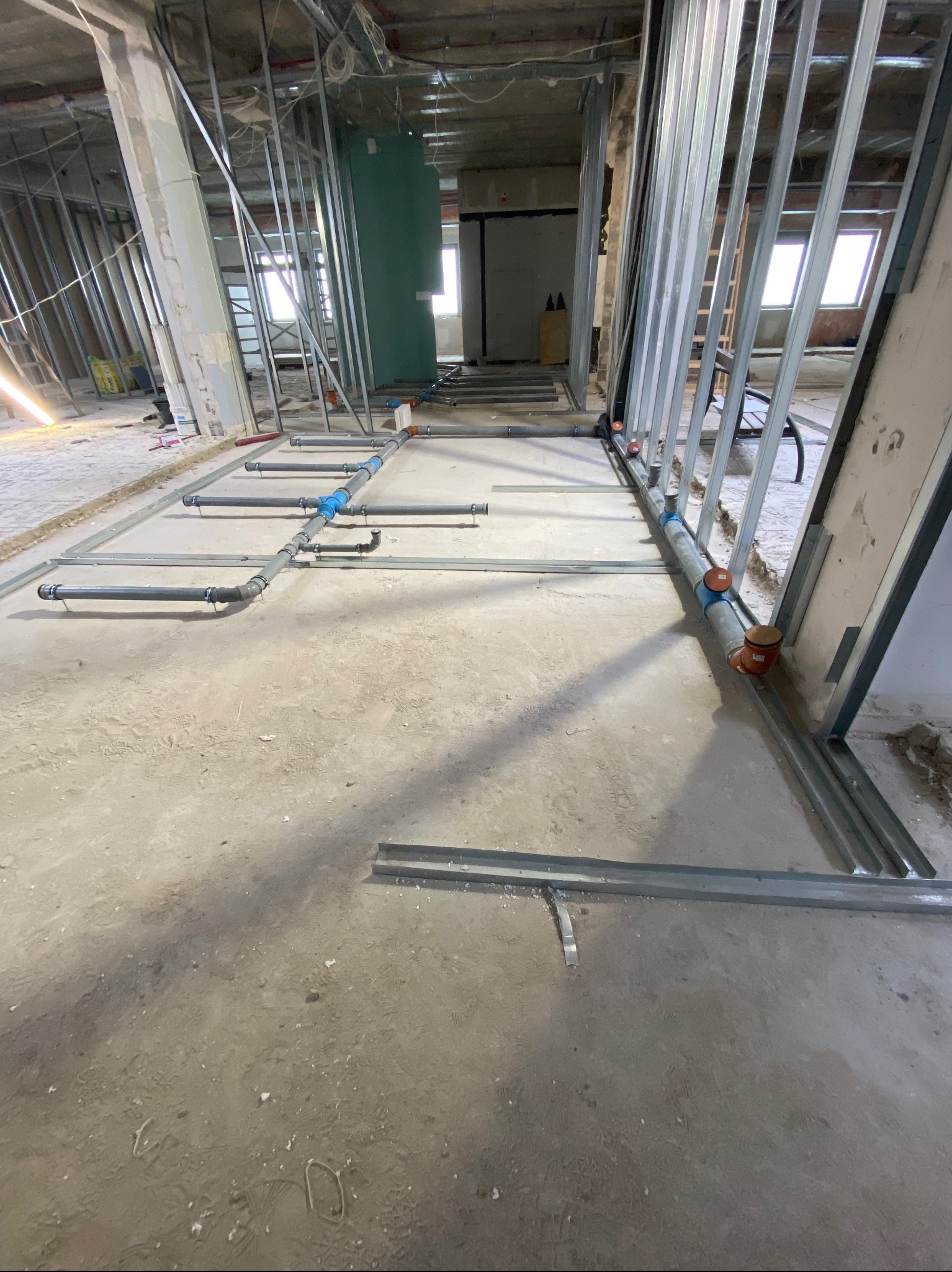 Instalacja rur kanalizacyjnych w surowym wnętrzu budynku w Poznaniu. Widoczne szare rury i metalowe profile konstrukcyjne ścian działowych. Etap prac instalacyjnych.