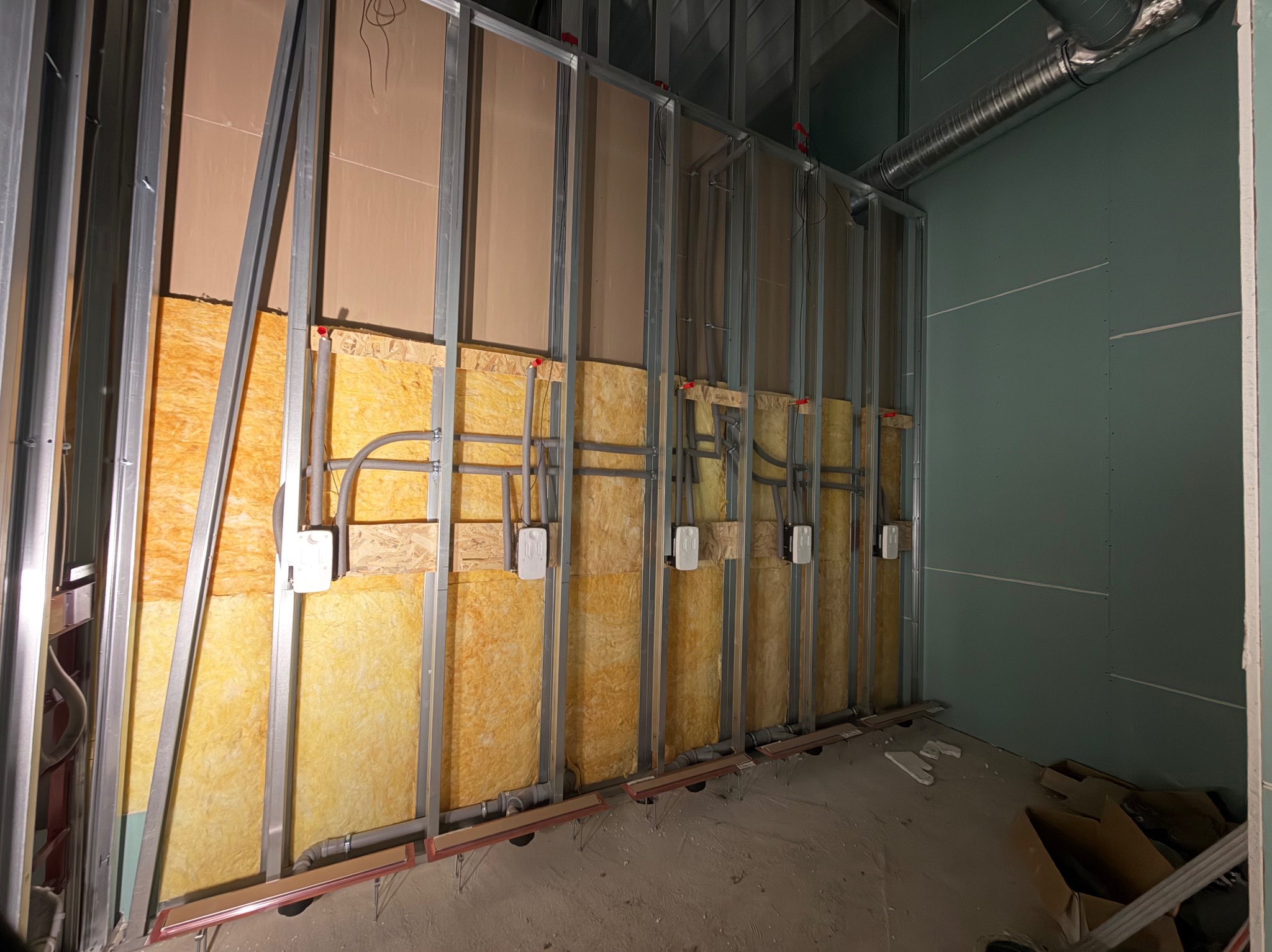 Ściana z izolacją z wełny mineralnej, profile stalowe, instalacja elektryczna w puszkach, rury wentylacyjne. Etap prac wykończeniowych wewnątrz budynku.