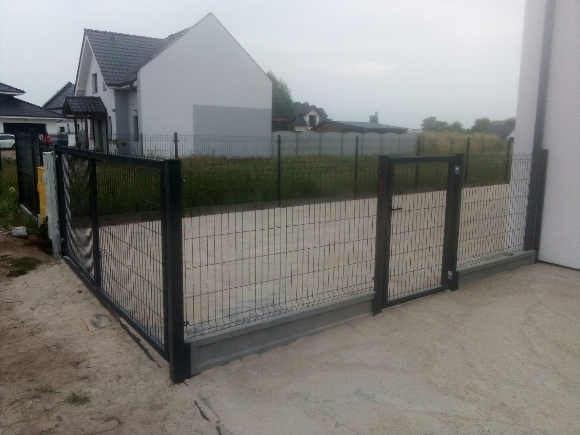 Nowoczesne, grafitowe ogrodzenie z siatki z furtką na betonowej podmurówce, widok na dom w tle.