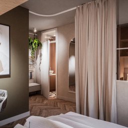 sueños studio - Nowoczesna sypialnia z widokiem na łazienkę przez szklaną ścianę i zasłony, na ścianie grafika w ramie, parkiet w jodełkę, szary fotel.