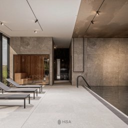 sueños studio - Wnętrze luksusowego spa z basenem i sauną, widoczne leżaki, duże okna z widokiem na zieleń, szara kamienna okładzina ścian i sufitu, minimalistyczne oświetlenie punktowe.