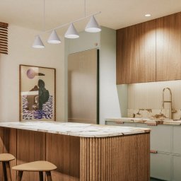 sueños studio - Nowoczesna kuchnia z wyspą, drewnianymi szafkami i marmurowym blatem, oświetlona czterema stożkowymi lampami wiszącymi.