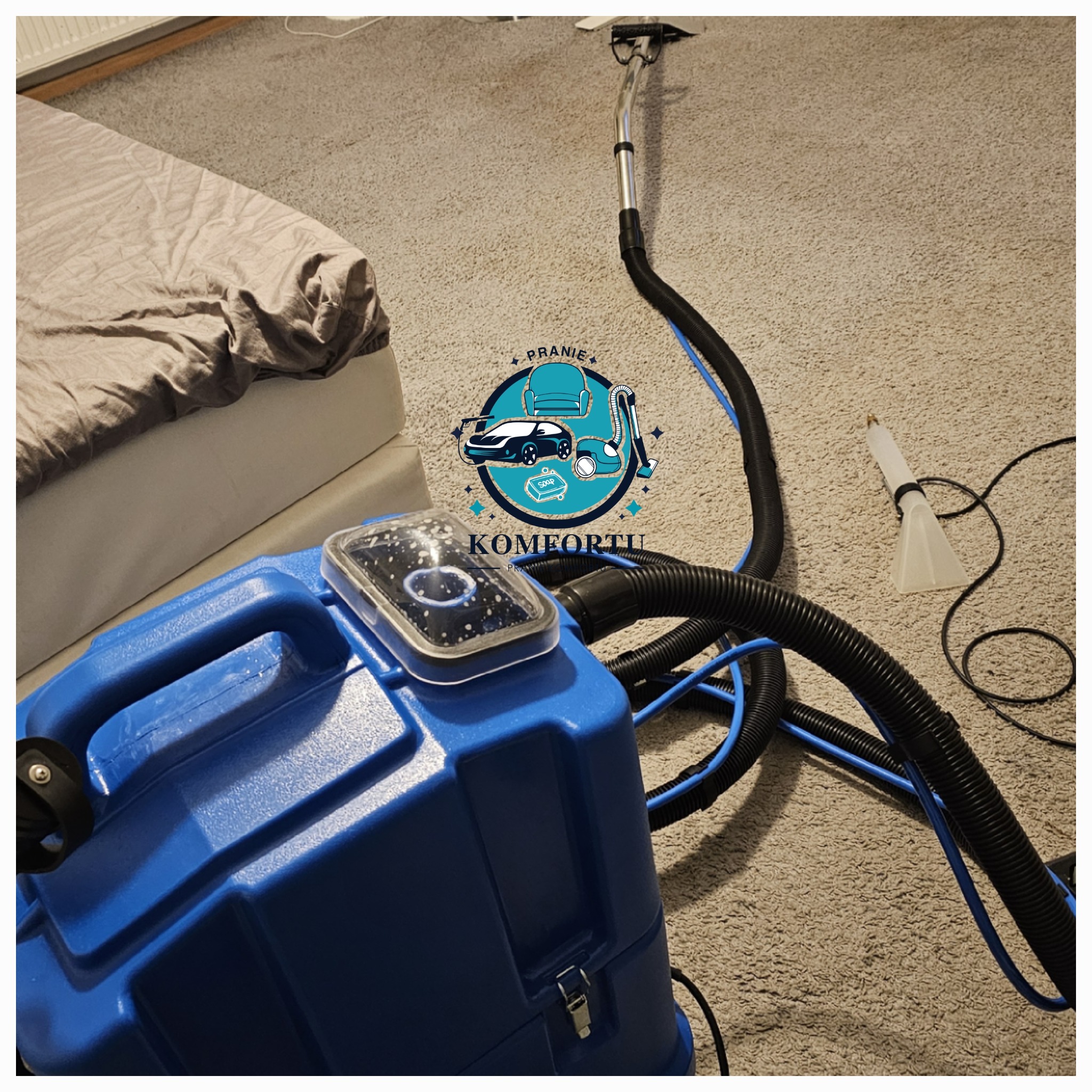 Narożnik łóżka oraz urządzenie do czyszczenia dywanów z logiem firmy, w trakcie pracy na beżowym dywanie.