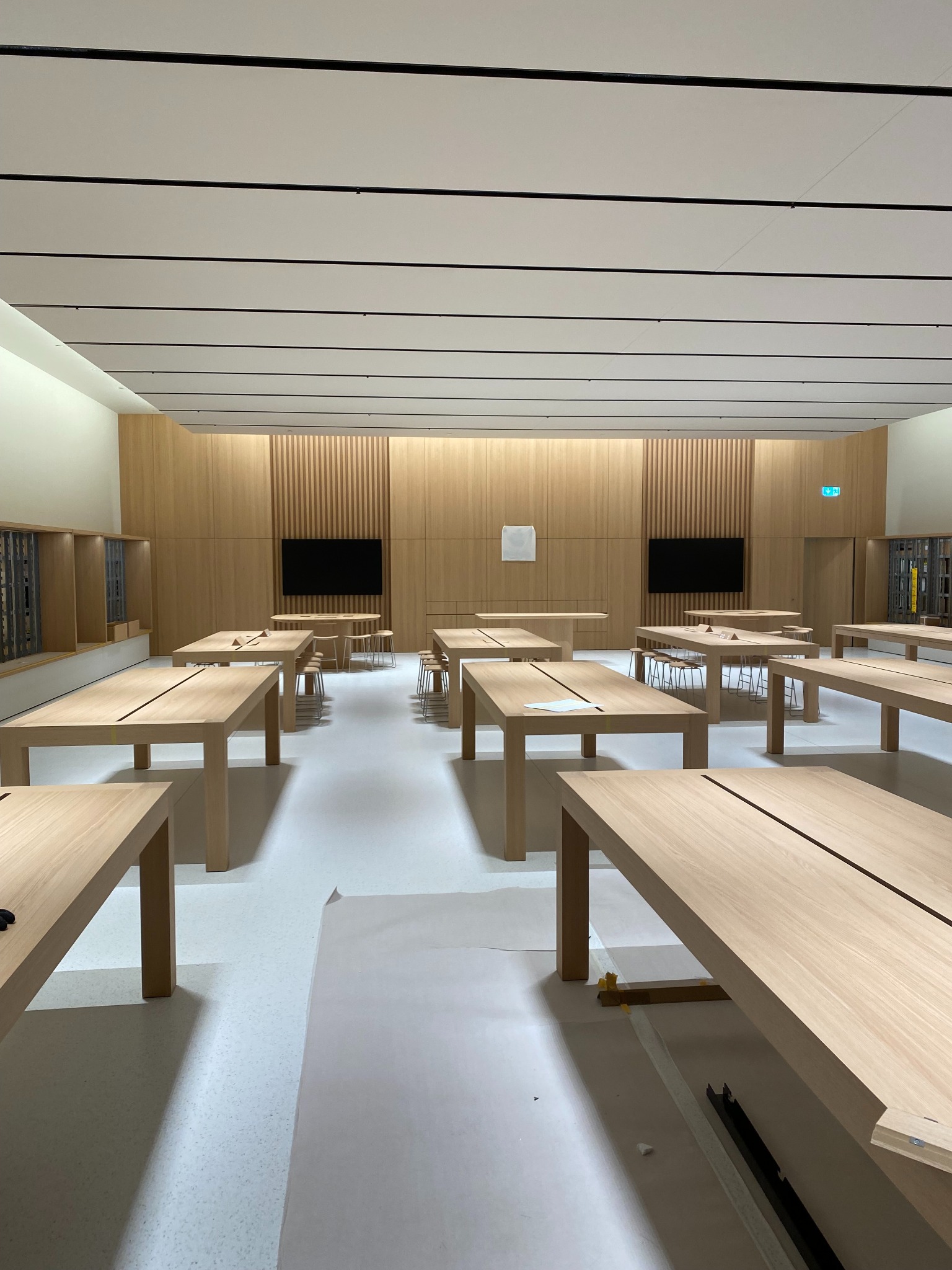 Montaż drewnianych paneli ściennych w nowoczesnym biurze z jasnymi meblami i białymi podłogami, widoczne zabezpieczenia podłoża folią malarską.