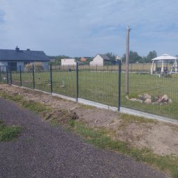 Kuba mąkosa - Nowoczesne ogrodzenie panelowe z podmurówką betonową, widok z boku, na tle domów jednorodzinnych i zielonego trawnika. Słoneczny dzień, błękitne niebo.