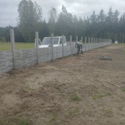 Kuba mąkosa - Montaż ogrodzenia betonowego z elementami dekoracyjnymi. Widoczny pracownik z łopatą, częściowo ukończony płot i samochód dostawczy w tle.