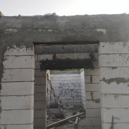 Kuba mąkosa - Surowy stan ściany z betonu komórkowego z widocznym nadprożem i śladami zaprawy, w tle drabina oparta o ścianę z graffiti. Etap budowy domu.