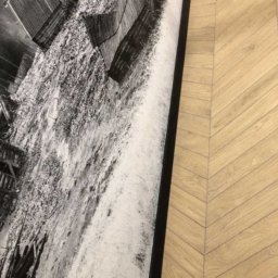 USŁUGI BUDOWLANO-REMONTOWE GRZEGORZ PAŹDZIORA - Fragment ściany z fototapetą przedstawiającą stare drewniane budynki na tle jasnej podłogi ułożonej w jodełkę.