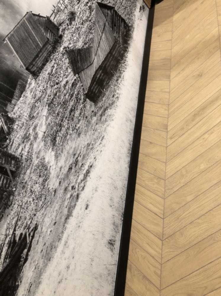 Fragment ściany z fototapetą przedstawiającą stare drewniane budynki na tle jasnej podłogi ułożonej w jodełkę.