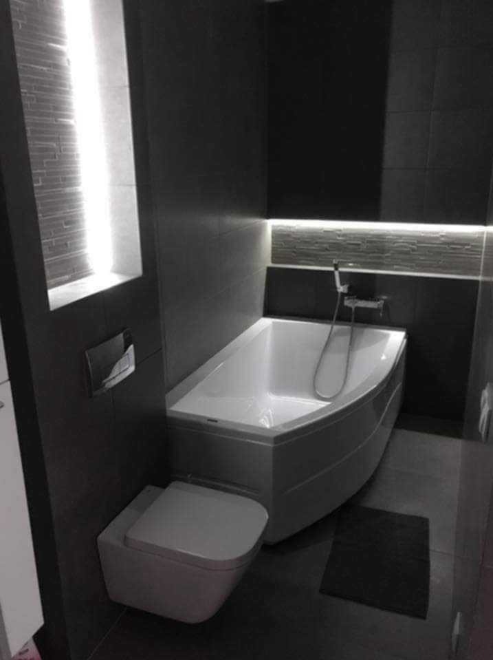 Nowoczesna łazienka w odcieniach szarości z narożną wanną, podświetleniem LED i podwieszaną toaletą.