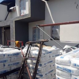 Hubert Szczepaniak - Nowa elewacja budynku w trakcie tynkowania, widoczne worki z zaprawą Knauf MP 75 L i rusztowanie.