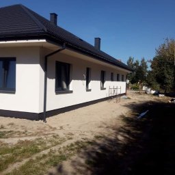 Hubert Szczepaniak - Świeżo pomalowana elewacja domu jednorodzinnego w Żyrardowie, z widocznymi czarnymi detalami wykończeniowymi, takimi jak rynny i obramowania okien, na tle błękitnego nieba.