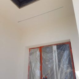 Hubert Szczepaniak - Wnętrze w trakcie prac wykończeniowych: ściana po nałożeniu gładzi, zabezpieczone folią okno i widoczny fragment okna dachowego.