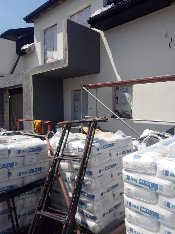 Nowa elewacja budynku w trakcie tynkowania, widoczne worki z zaprawą Knauf MP 75 L i rusztowanie.