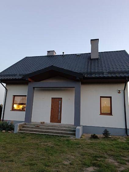 Nowoczesny dom jednorodzinny z szarą dachówką, białymi ścianami i grafitowymi elementami wykończeniowymi, widok z poziomu gruntu, zachód słońca.