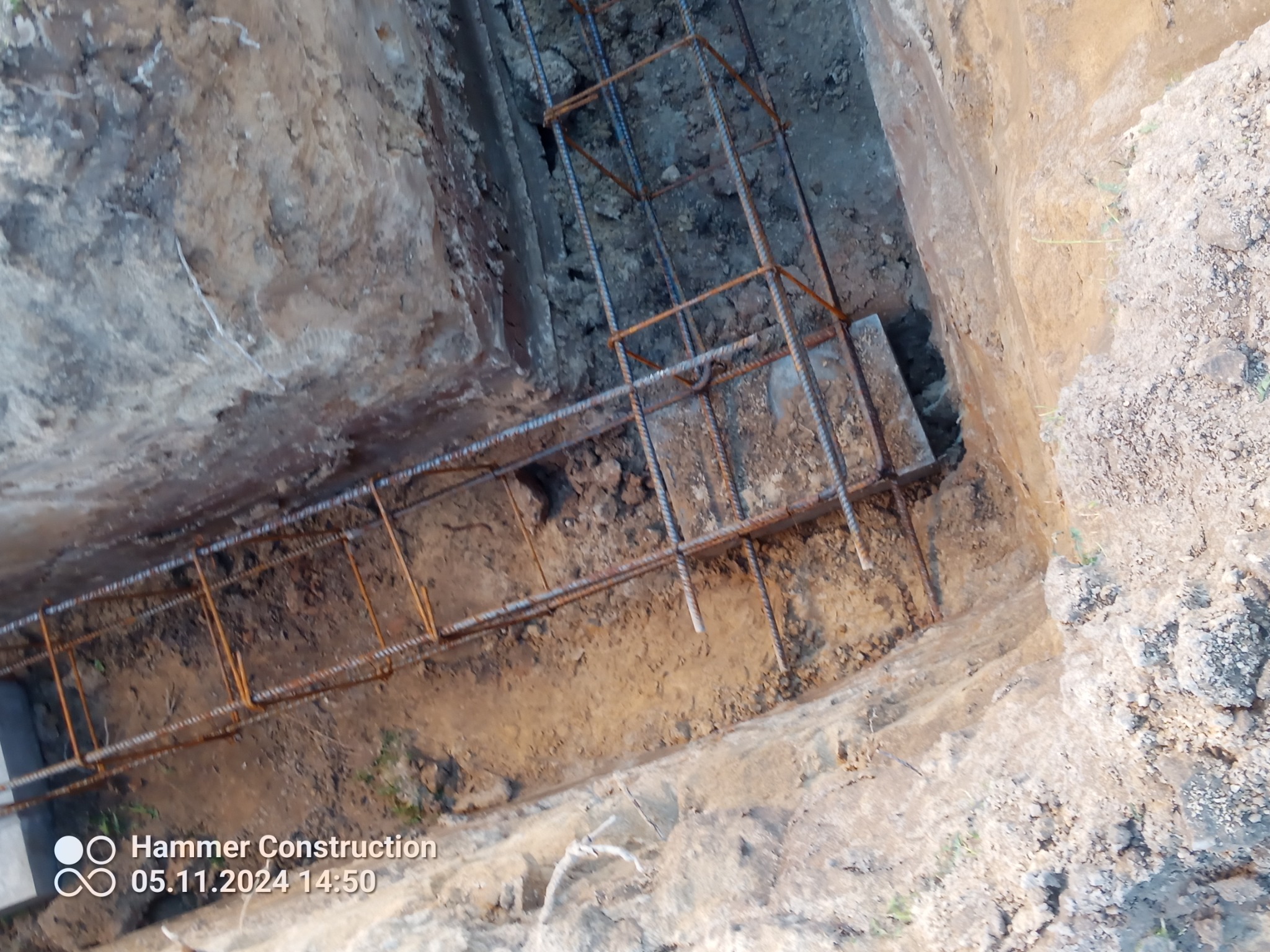 Zbrojenie ławy fundamentowej w wykopie, widoczne pręty zbrojeniowe połączone w konstrukcję szkieletową, ziemia wokół wykopu.