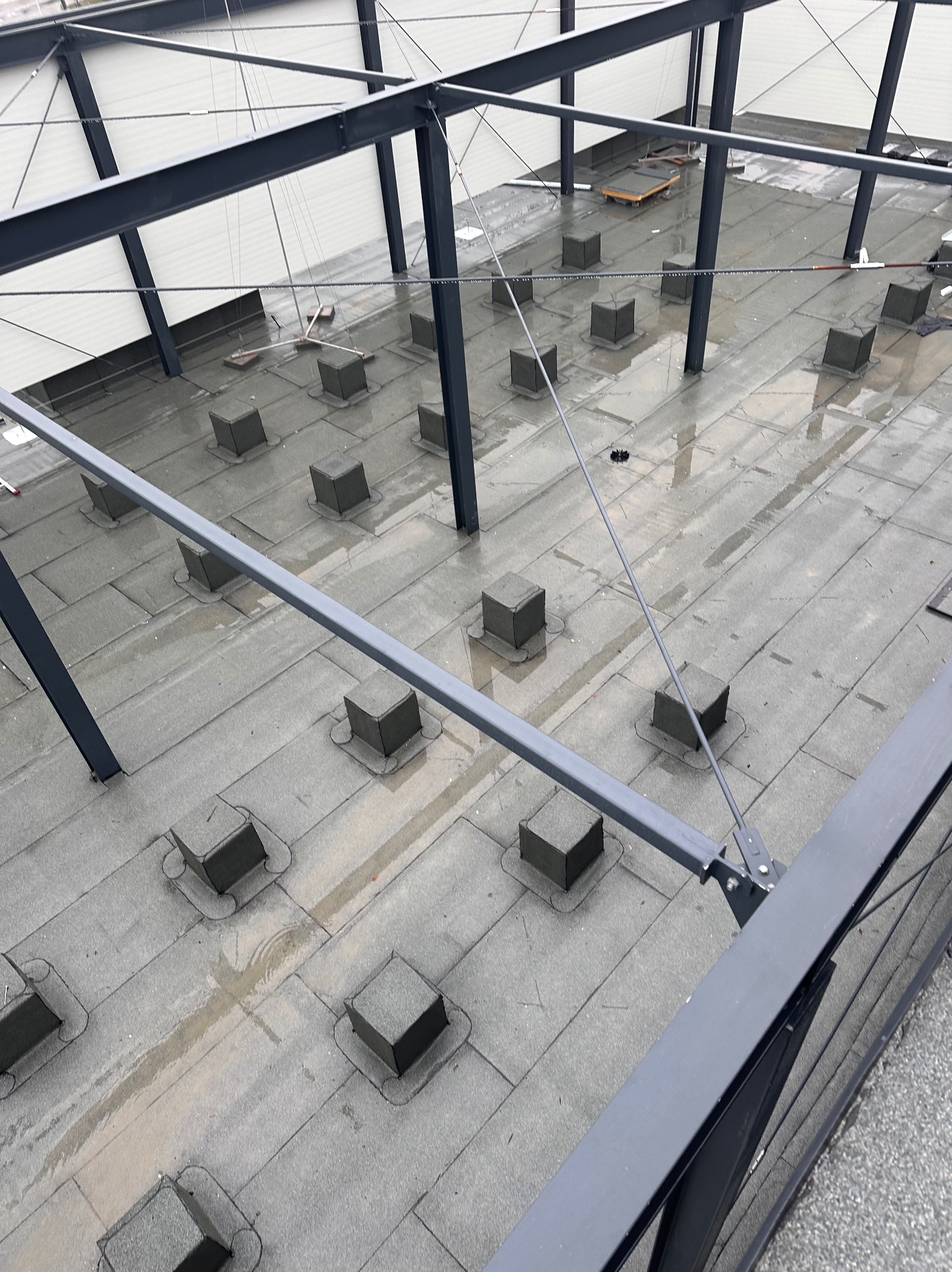 Płaski dach pokryty papą z licznymi kominkami wentylacyjnymi w kształcie sześcianów, widok z góry na metalową konstrukcję budynku.