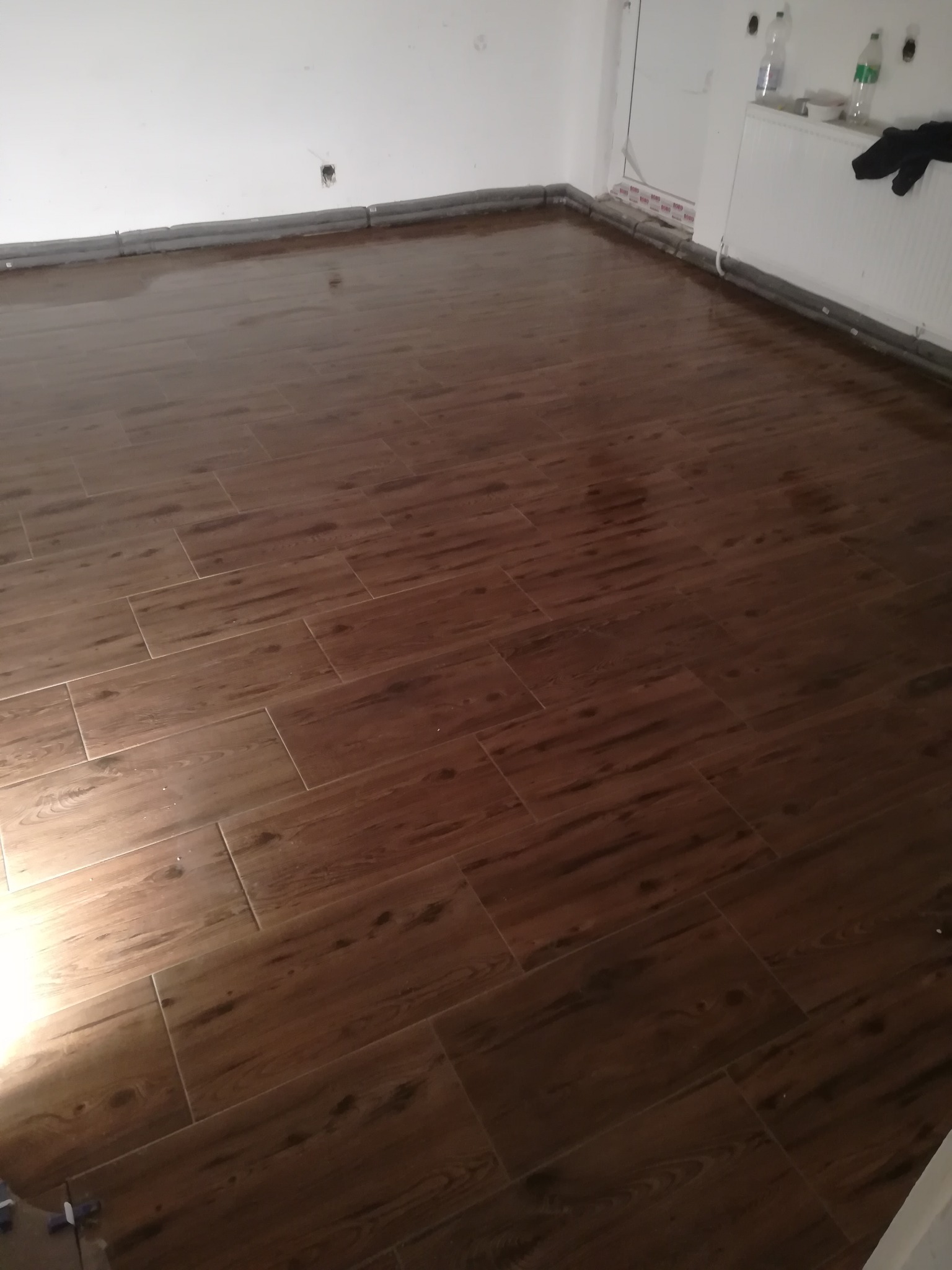 Ukończona podłoga z paneli imitujących drewno w jasnym pomieszczeniu, widoczne listwy przypodłogowe i grzejnik.