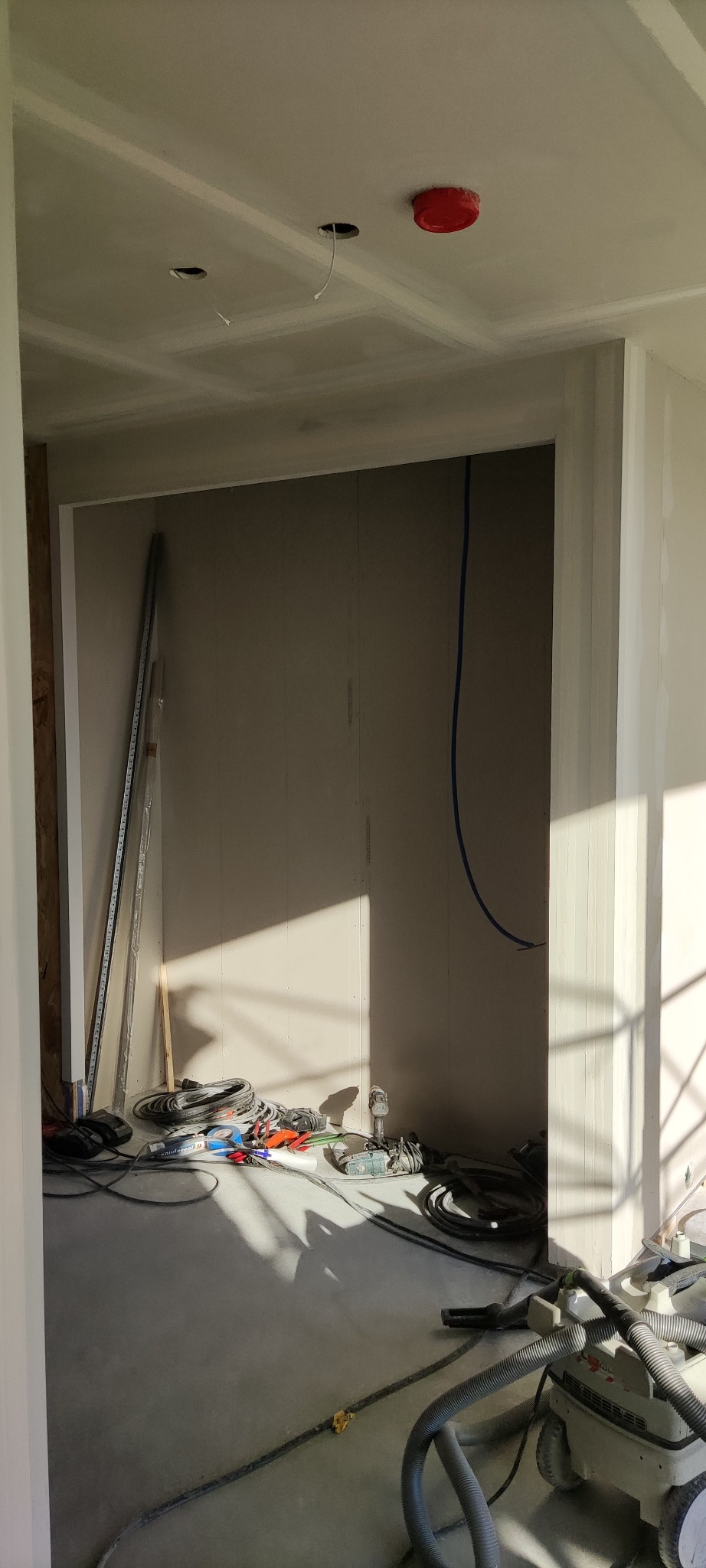 Wnętrze w trakcie remontu: ściany z płyt gipsowo-kartonowych, widoczna instalacja elektryczna, narzędzia budowlane i odkurzacz przemysłowy, przygotowanie do gładzi.