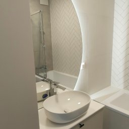 PROFIHOME & OLEKSANDR MELESHKO - Nowoczesna łazienka z owalną umywalką nablatową, podświetlanym lustrem i białymi płytkami ułożonymi w jodełkę.