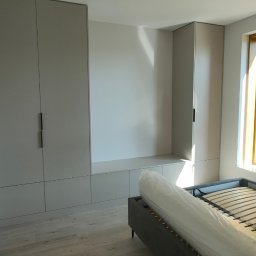 PROFIHOME & OLEKSANDR MELESHKO - Wnętrze pokoju z zabudową meblową w odcieniach szarości, łóżko z drewnianym stelażem i widokiem na zieleń przez okno.