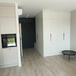 PROFIHOME & OLEKSANDR MELESHKO - Jasne wnętrze mieszkania z zabudową kuchenną, szafami wnękowymi i minimalistycznym stolikiem kawowym na tle parkietu.