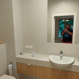 PROFIHOME & OLEKSANDR MELESHKO - Jasna łazienka z beżowymi płytkami podłogowymi, wiszącą szafką pod umywalką z drewnianymi frontami i dużym lustrem, w którym odbija się osoba robiąca zdjęcie.