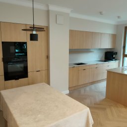 PROFIHOME & OLEKSANDR MELESHKO - Jasna, nowoczesna kuchnia z drewnianymi szafkami, wyspą z białym blatem i parkietem w jodełkę. Czarny piekarnik w zabudowie i minimalistyczne lampy wiszące.