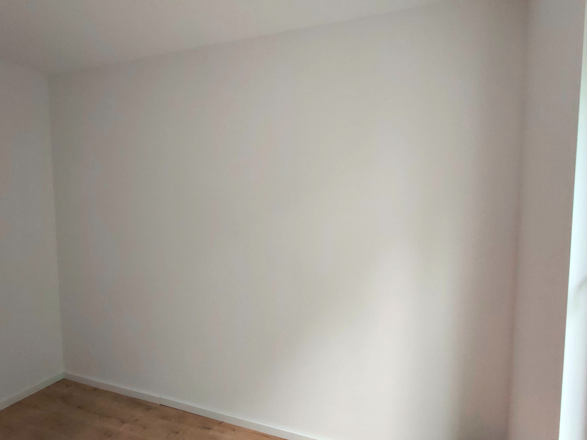 Pomalowane na biało ściany w rogu pokoju z drewnianą podłogą i białą listwą przypodłogową.