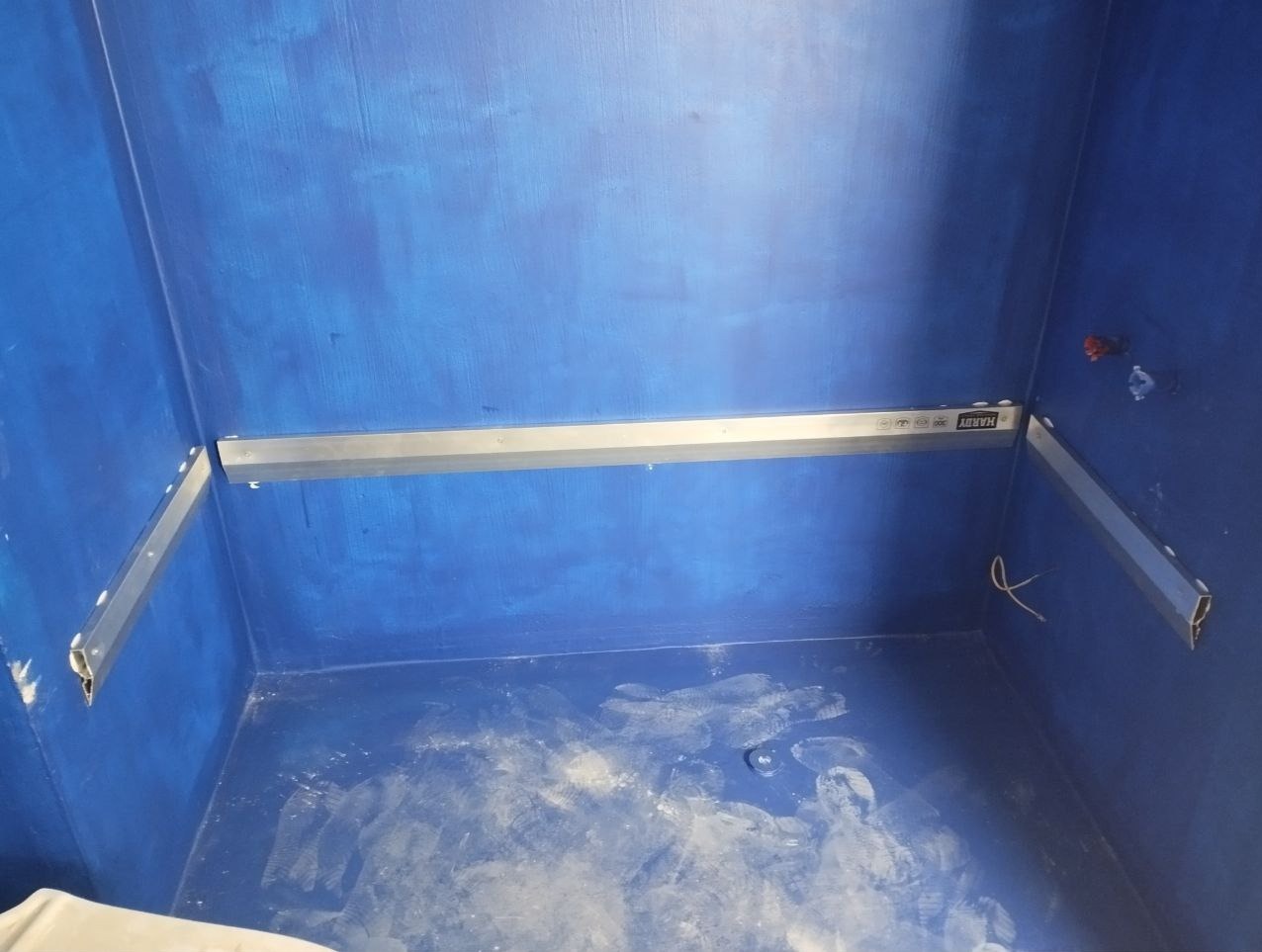 Niebieska hydroizolacja w kabinie prysznicowej ze wspornikami poziomującymi Hardy zamontowanymi na ścianach, przygotowanie do montażu płytek.