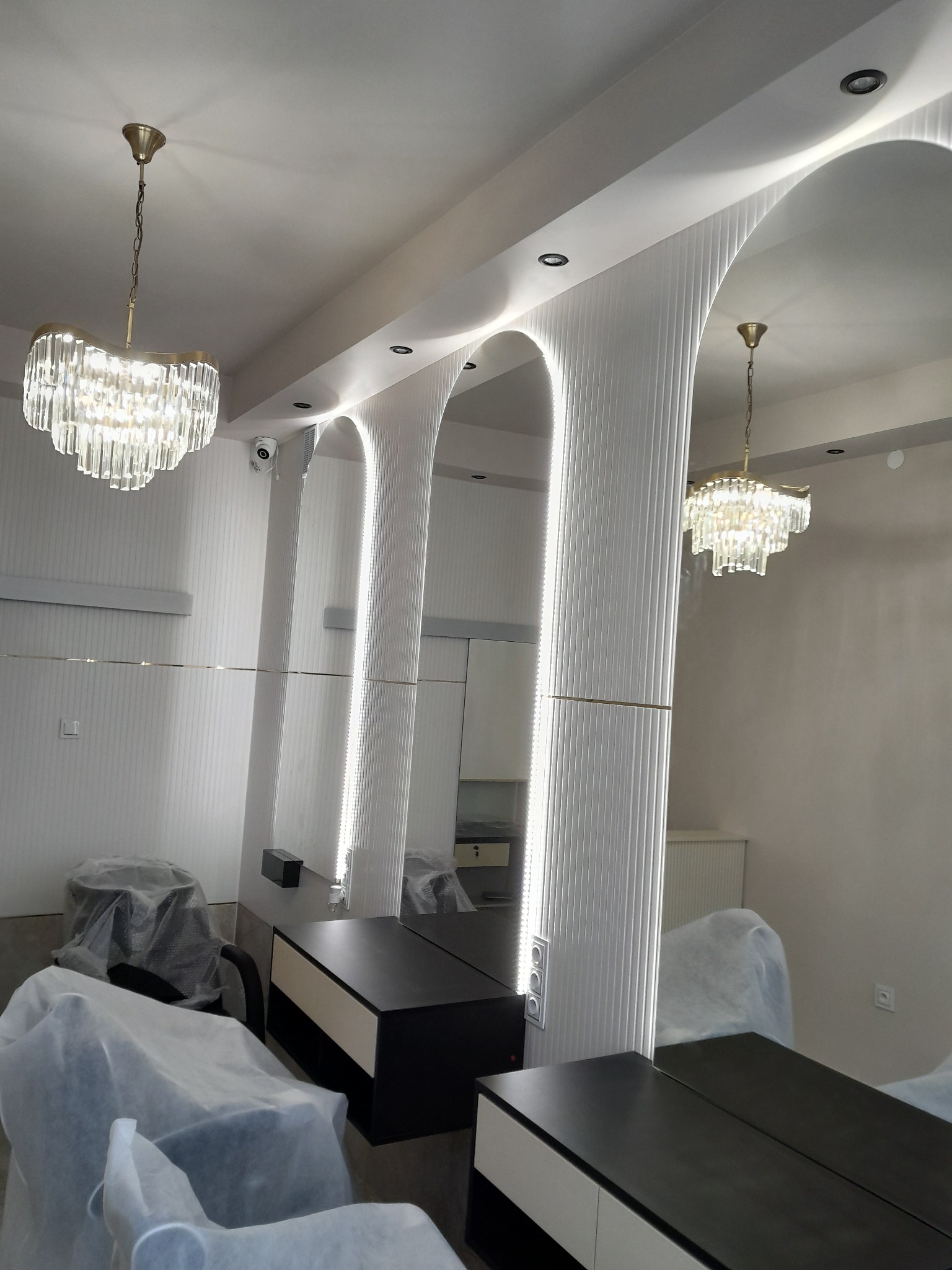 Nowoczesne wykończenie wnętrza salonu fryzjerskiego z lustrami w kształcie łuków i oświetleniem LED. Krzesła zabezpieczone folią ochronną.