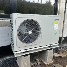 F.U.H. EFEKT ADAM GAWLAK, STANISŁAW GAWLAK SPÓŁKA CYWILNA - Pompa ciepła Beretta Monoblock 10 kW zamontowana na betonowych blokach przy ścianie budynku w trakcie budowy, widoczne okno i drzwi wejściowe, teren wokół w trakcie zagospodarowania.
