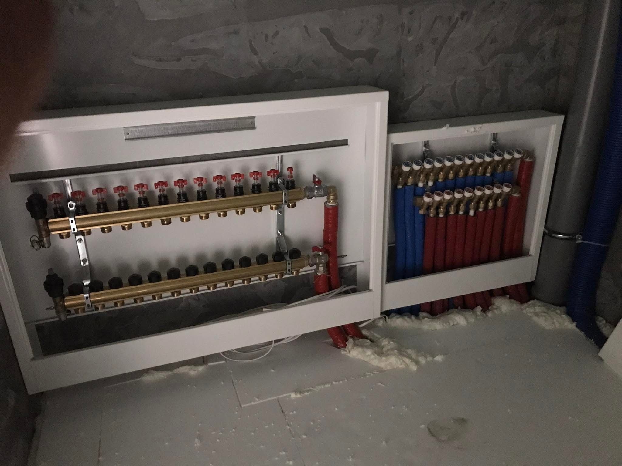 Rozdzielacz instalacji podłogowej w białej obudowie, widoczne rury czerwone i niebieskie, oraz skrzynka sterownicza firmy Tech dla wielu pomieszczeń, montaż w trakcie prac wykończeniowych.