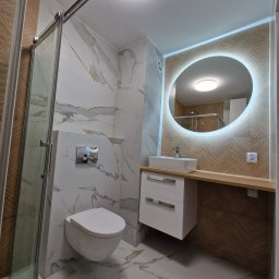 MARGO MARCIN GOC - Nowoczesna łazienka z marmurowymi płytkami, kabiną prysznicową ze szklanymi drzwiami, podwieszaną toaletą, szafką z umywalką nablatową i okrągłym lustrem z podświetleniem LED.