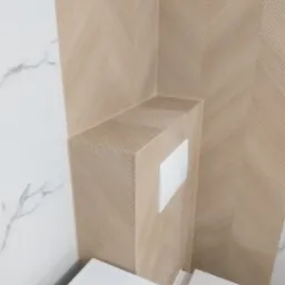 Fragment wykończonej łazienki z beżowymi płytkami ułożonymi we wzór jodełki na zabudowie stelaża WC i ścianie, oraz białymi płytkami imitującymi marmur po lewej stronie