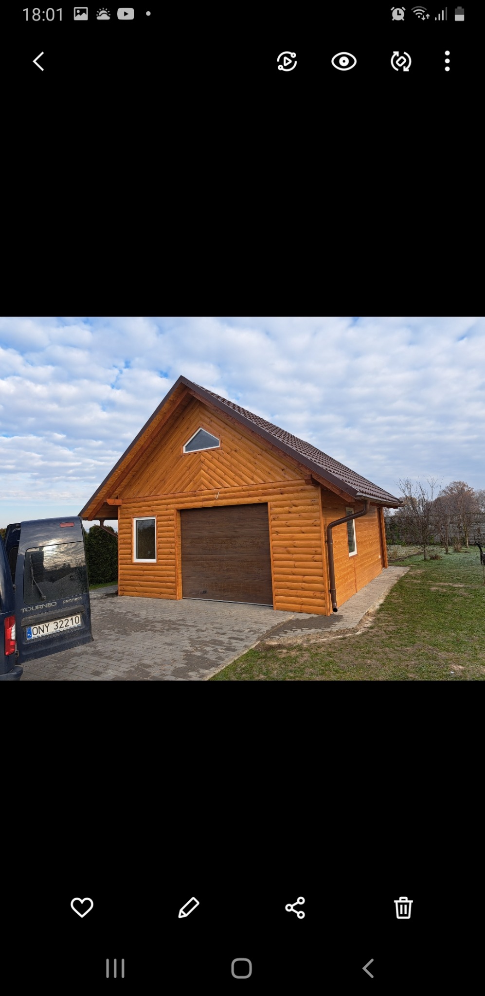 Nowy, drewniany garaż z brązową bramą segmentową, oknem w kształcie trójkąta w szczycie dachu i zaparkowanym samochodem dostawczym z otwartymi drzwiami z tyłu.