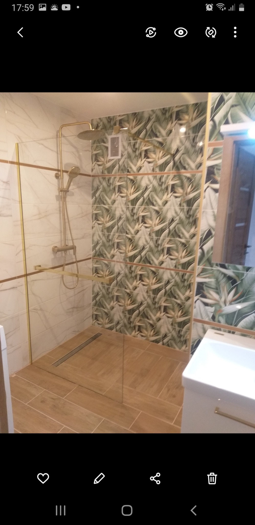 Nowoczesna kabina prysznicowa z deszczownicą w łazience wykończonej płytkami imitującymi marmur i tropikalne liście, z odpływem liniowym w podłodze.