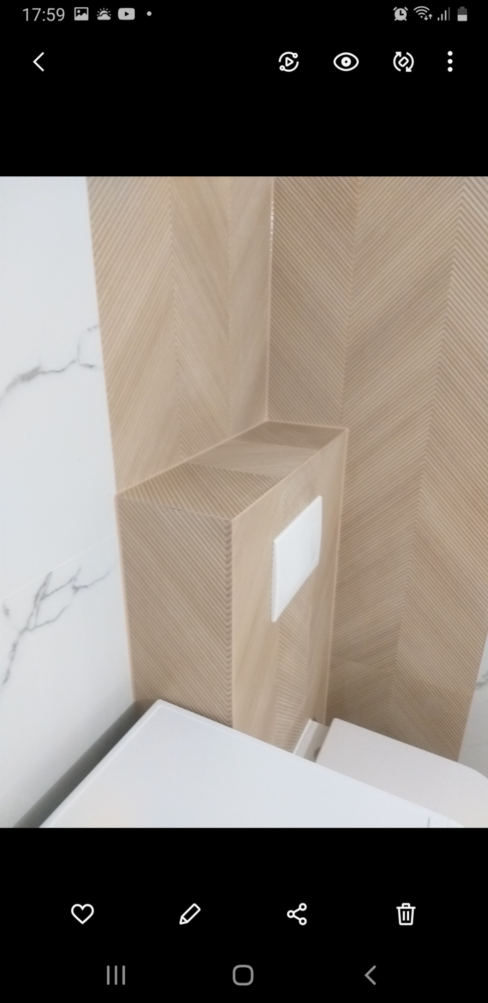 Fragment wykończonej łazienki z beżowymi płytkami ułożonymi we wzór jodełki na zabudowie stelaża WC i ścianie, oraz białymi płytkami imitującymi marmur po lewej stronie