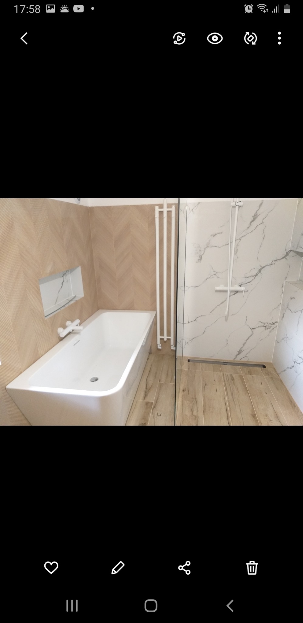 Nowoczesna łazienka z wanną, grzejnikiem drabinkowym, kabiną prysznicową z marmurowymi płytkami i drewnopodobną podłogą, wykończona w jasnych, stonowanych kolorach.