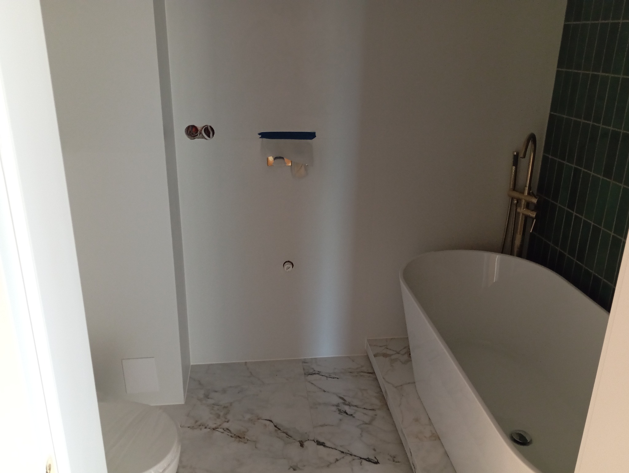 Wnętrze łazienki w trakcie prac wykończeniowych:  wolnostojąca wanna, marmurowe płytki podłogowe, ściany przygotowane pod montaż armatury, widoczne puszki elektryczne i  taśma malarska...