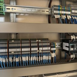 EL-MATIC - Rozdzielnica elektryczna z uporządkowanymi przewodami oznaczonymi etykietami, listwy zaciskowe Wago, styczniki Siemens Sirius i przewody ochronne żółto-zielone, zamontowane na szynach DIN w szarej...