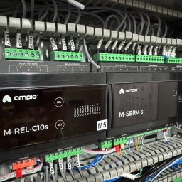 EL-MATIC - Rozdzielnica elektryczna z modułami sterującymi Ampio M-REL-C10s i M-SERV-s, widoczne liczne przewody, złącza śrubowe i oznaczenia.