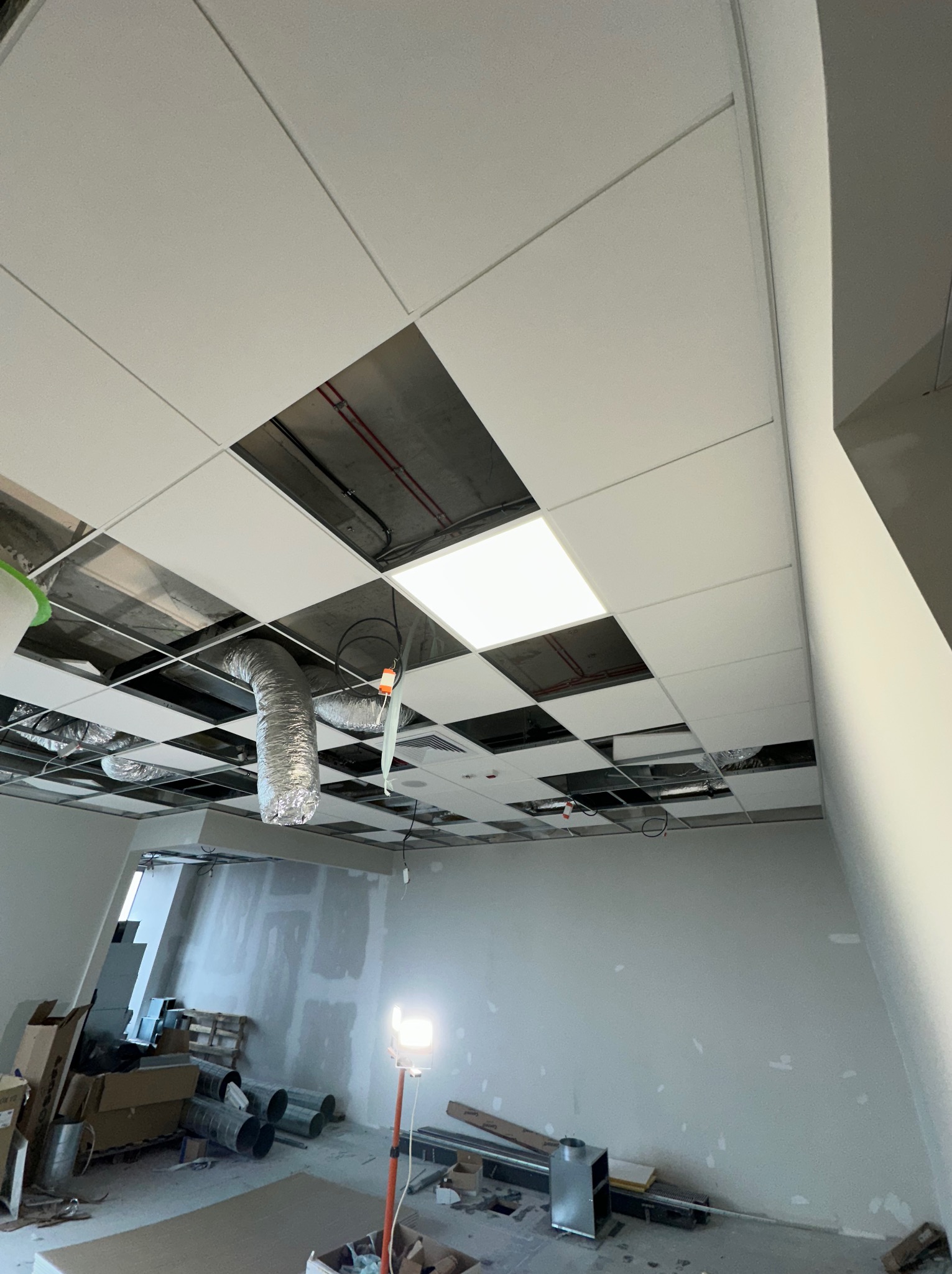 Montaż sufitu podwieszanego z widocznymi elementami instalacji wentylacyjnej i elektrycznej w przestrzeni biurowej w trakcie prac wykończeniowych.
