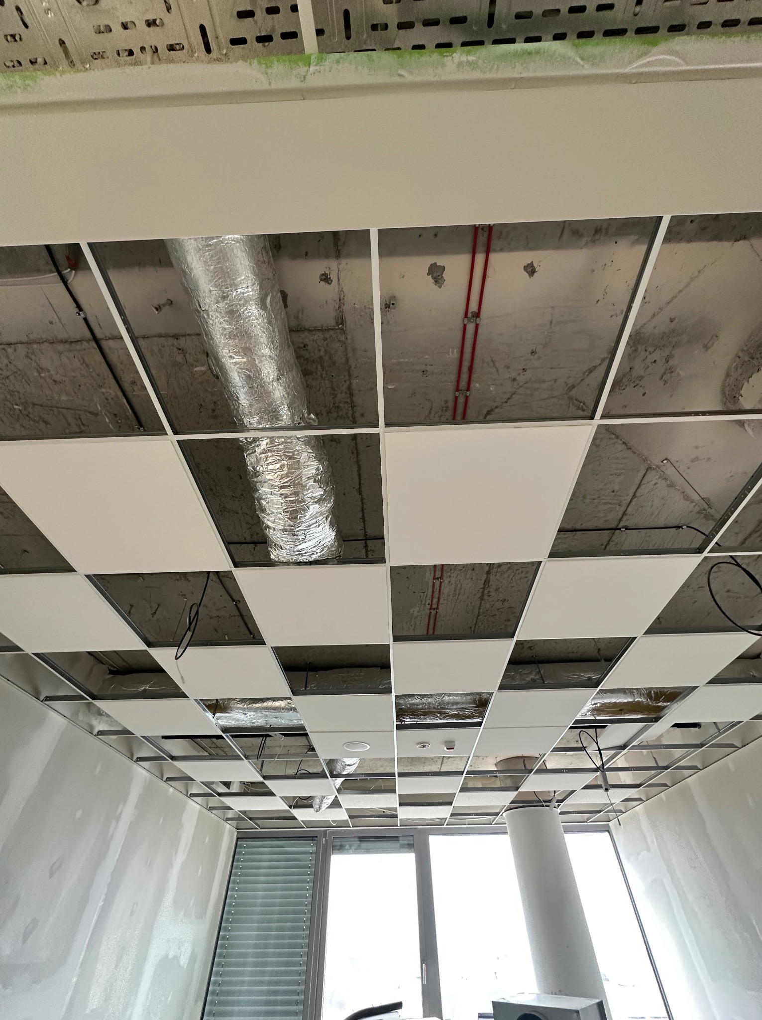 Sufit podwieszany kasetonowy w trakcie montażu, widoczne elementy instalacji wentylacyjnej i elektrycznej, ściany w trakcie prac wykończeniowych.