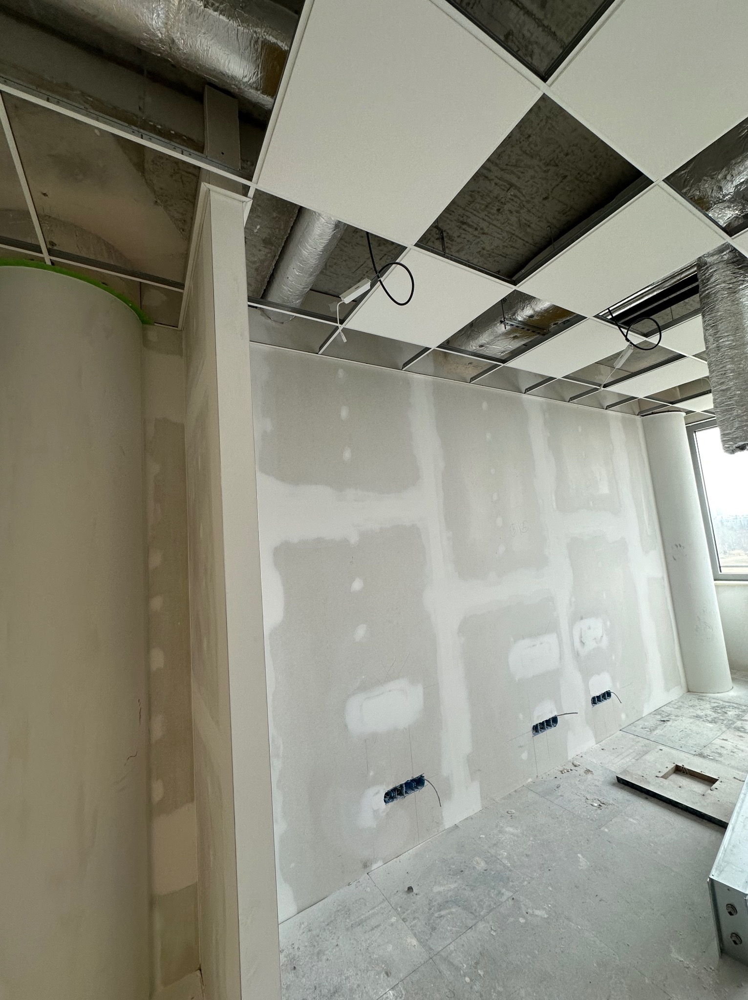 Wnętrze biurowe w trakcie prac wykończeniowych: ściany z płyt gipsowo-kartonowych z widocznymi miejscami łączeń i otworami na gniazdka elektryczne, sufit podwieszany kasetonowy z instalacjami...