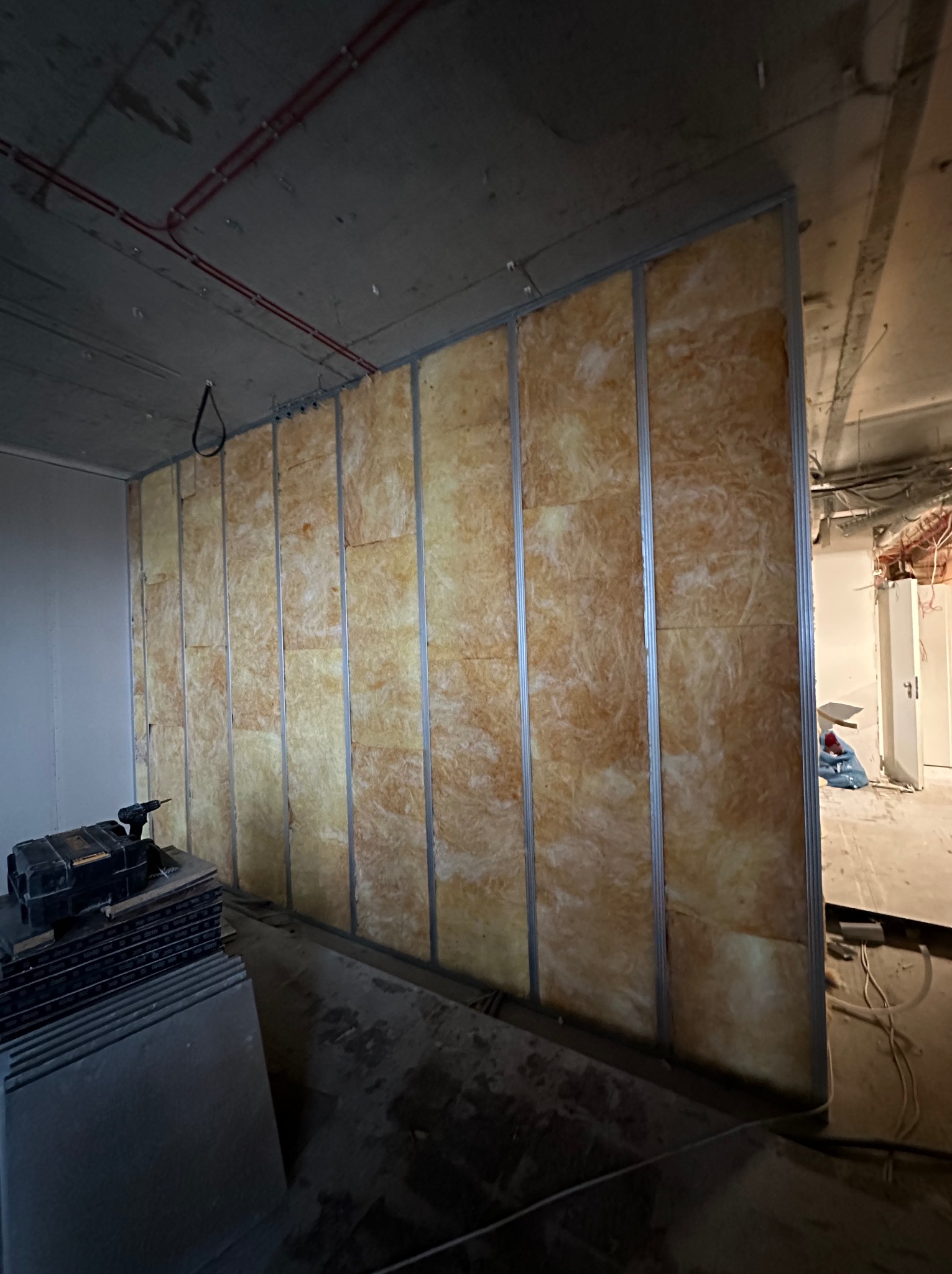 Montaż izolacji z wełny mineralnej w metalowej konstrukcji szkieletowej, przygotowanej pod obłożenie płytami. W tle widoczne narzędzia i materiały budowlane.