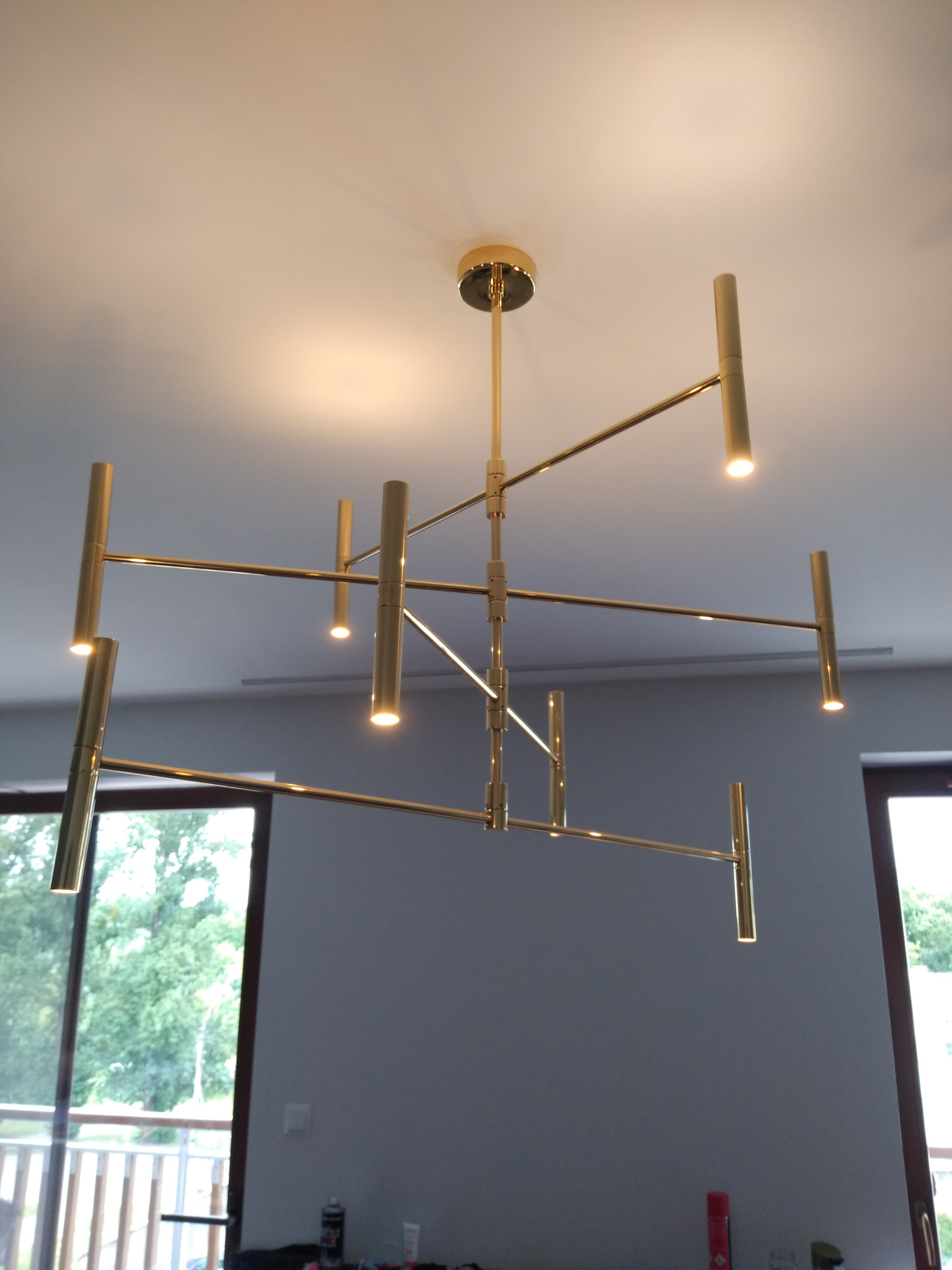 Złota, nowoczesna lampa sufitowa z punktowymi źródłami światła, zamontowana w jasnym pomieszczeniu z oknami. Widok z dołu, podkreślający geometryczny design.